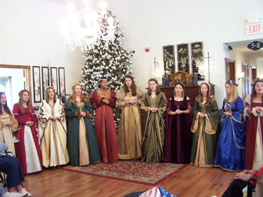 A group of performers dressed in colorful traditional gowns singing in front of a decorated Christmas tree.