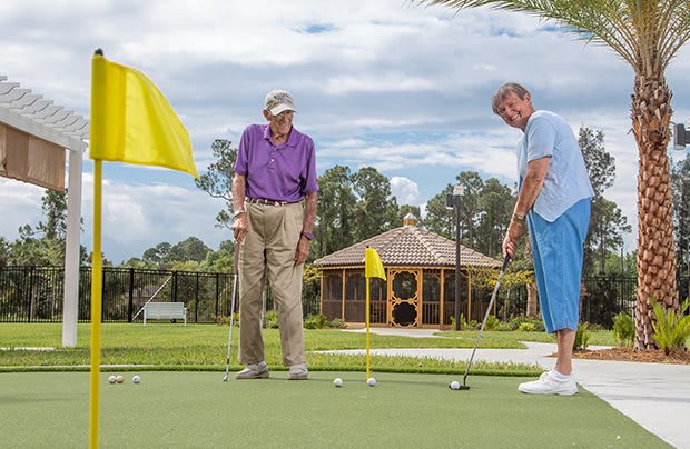 Two elderly men enjoying a game of golf on a putting green.
