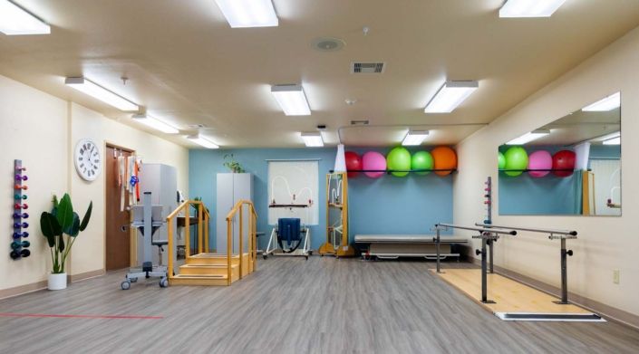 A spacious rehabilitation center equipped with therapy balls, parallel bars, and other physical therapy tools.