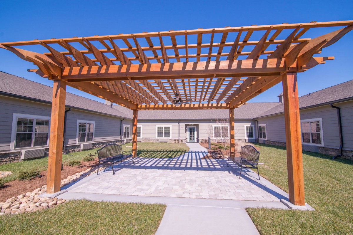 A spacious courtyard with a wooden pergola and outdoor seating on a sunny day.