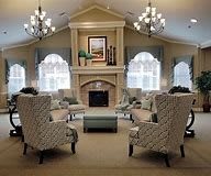 A cozy and elegant living room featuring a central fireplace, armchairs, and chandeliers.