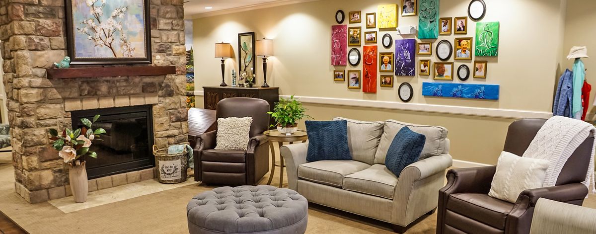 A cozy living room with a sofa, armchair, ottoman, and colorful wall art.
