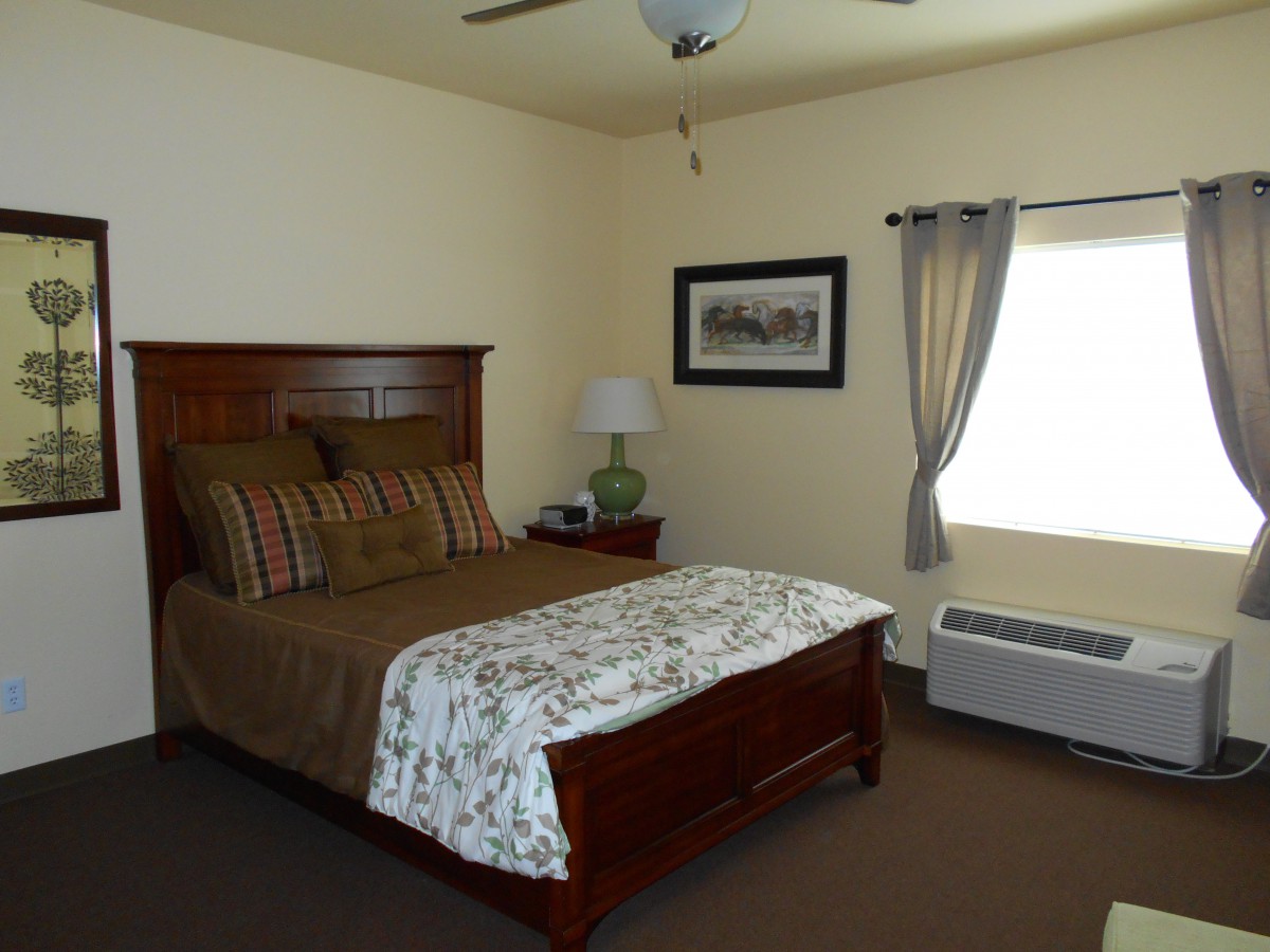 A cozy bedroom with a wooden bed frame, decorative bedding, a bedside lamp, and a window with curtains.
