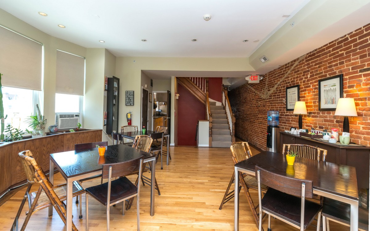 A cozy dining area with multiple tables and chairs, featuring a wooden floor and exposed brick walls.