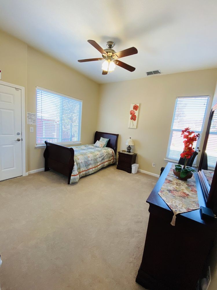 A cozy bedroom with a single bed, ceiling fan, and floral decorations.