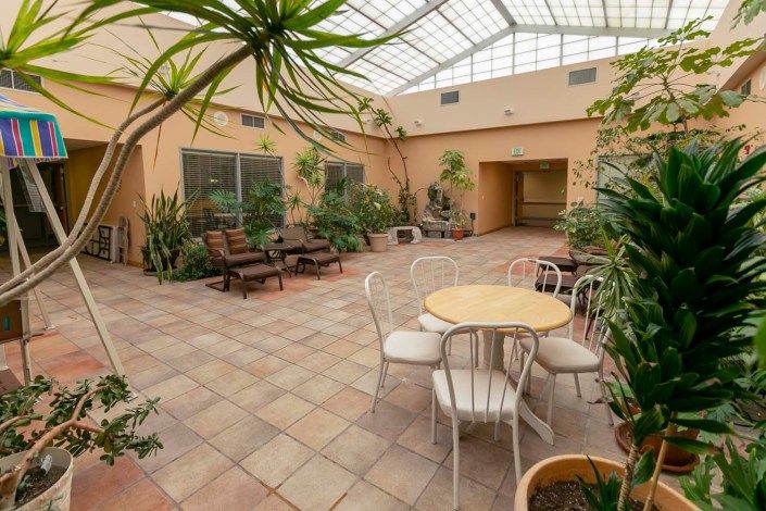 A serene indoor courtyard with a skylight, featuring potted plants, a round table with chairs, and comfortable seating.