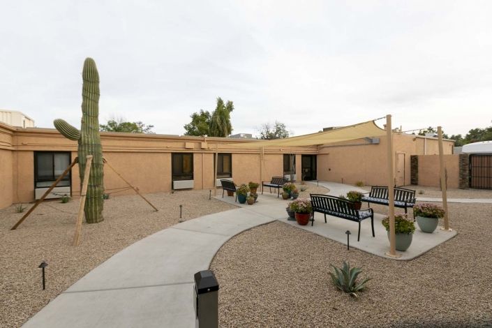 A desert courtyard with a cactus, outdoor seating, and a building in the background.