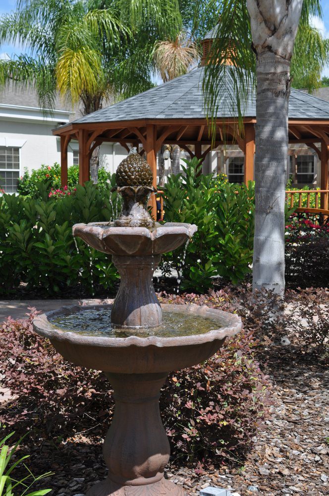 A tranquil garden setting featuring a tiered fountain and a wooden gazebo surrounded by lush greenery.