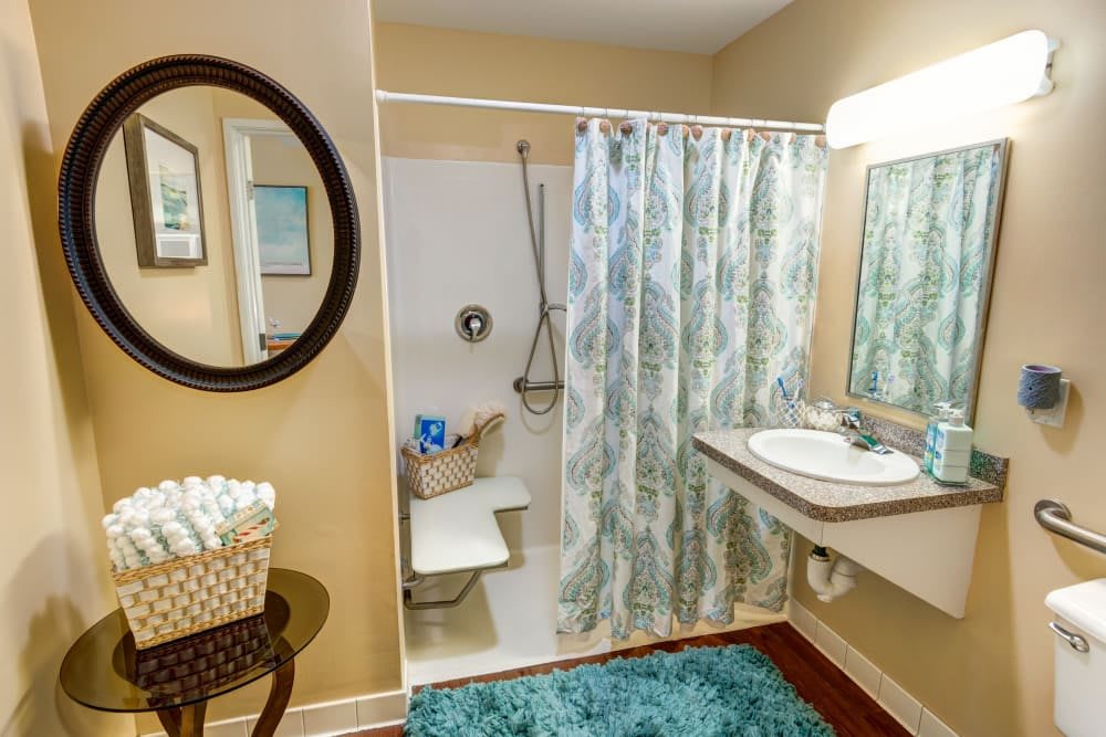 A cozy bathroom featuring a shower with a patterned curtain, a sink with a mirror above it, and a basket of towels.