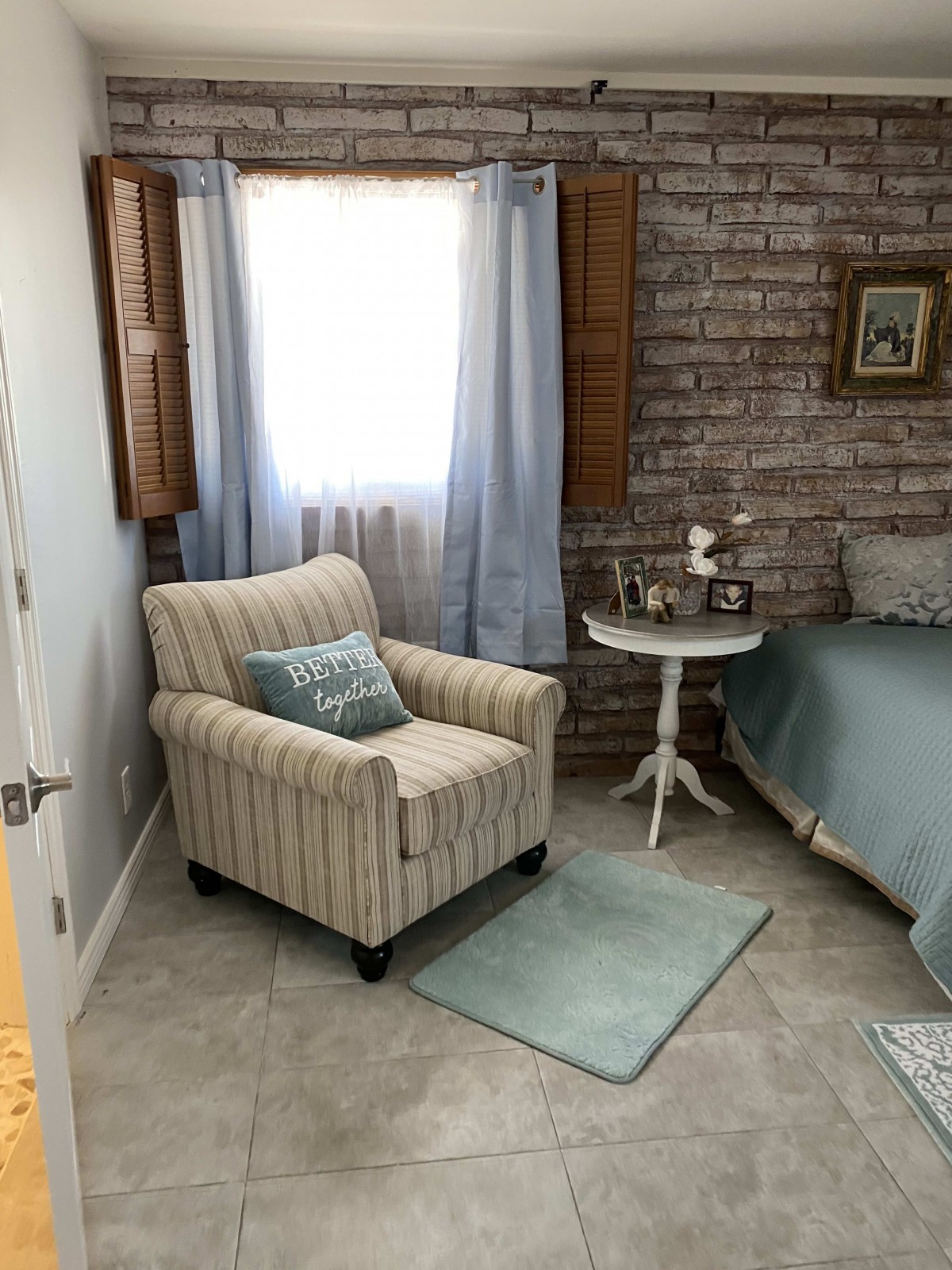 A cozy bedroom corner featuring an armchair, side table, and brick wall.