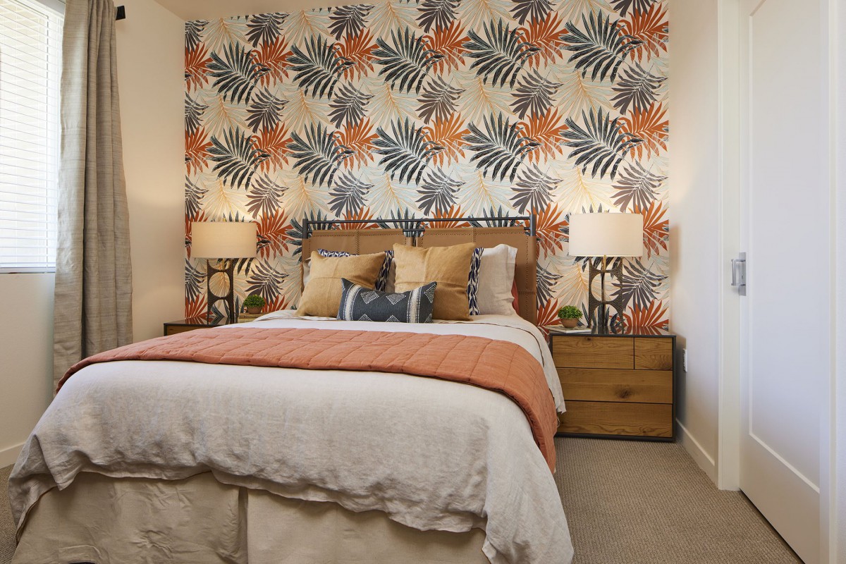 A stylish bedroom with vibrant floral wallpaper, a neatly made bed, and matching bedside lamps.