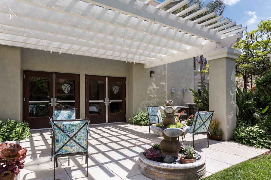 A sunny outdoor patio featuring a pergola, seating area, and a decorative fountain.