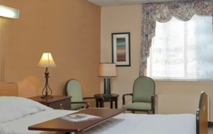 A cozy hotel room featuring a bed, two lamps, chairs, and a window with curtains.