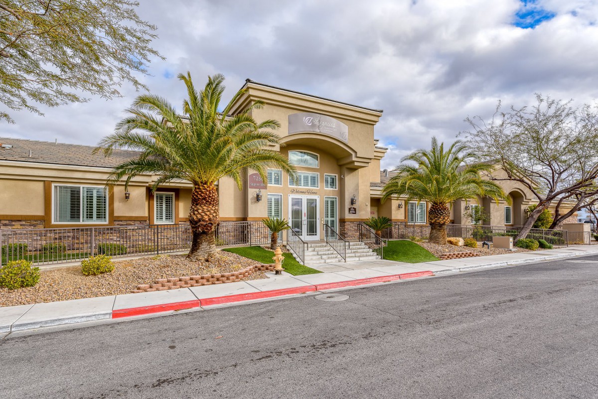 A view of a building entrance surrounded by palm trees and landscaped grounds under a cloudy sky.