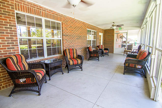 A covered patio with wicker furniture and a brick wall backdrop.