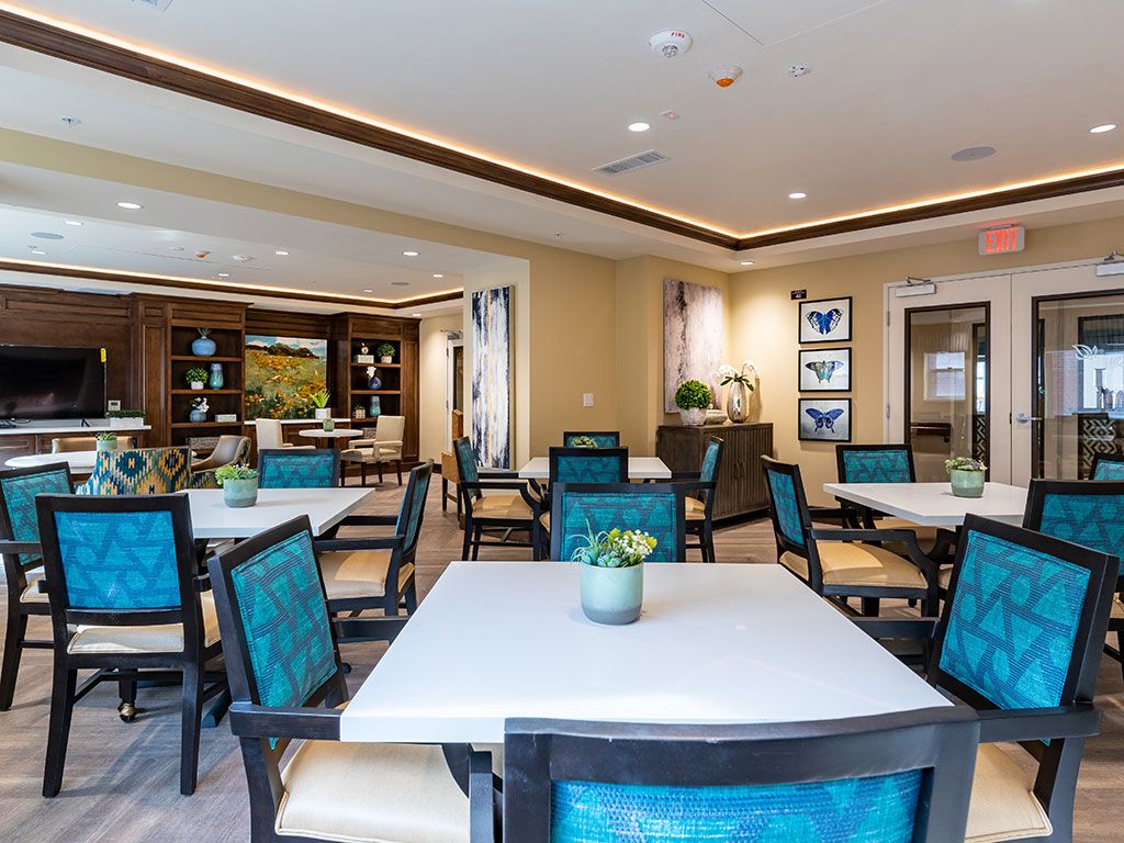 A modern indoor dining room with neatly arranged tables and chairs, featuring decorative plants and artwork.