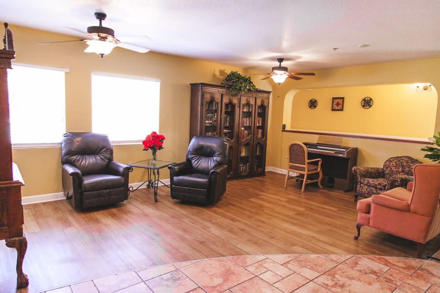 A cozy living room featuring recliner chairs, a wooden bookshelf, a small desk, and ceiling fans.