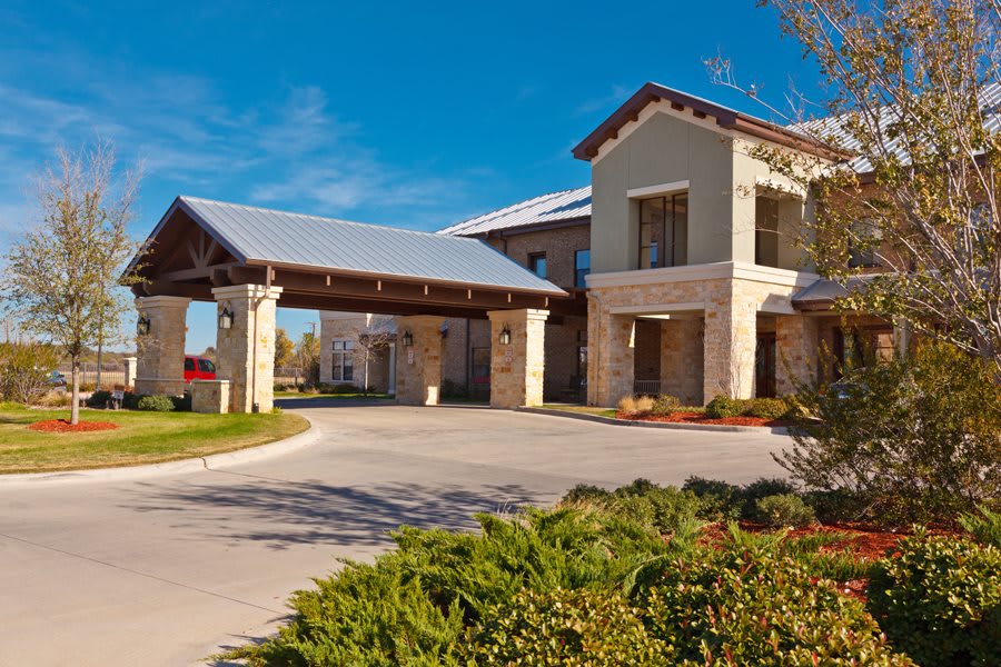 A modern building with a covered entrance and landscaped surroundings under a clear blue sky.