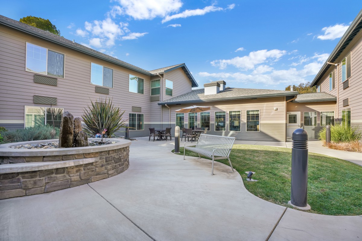 A residential building with an outdoor courtyard and landscaped garden area under a blue sky with clouds.