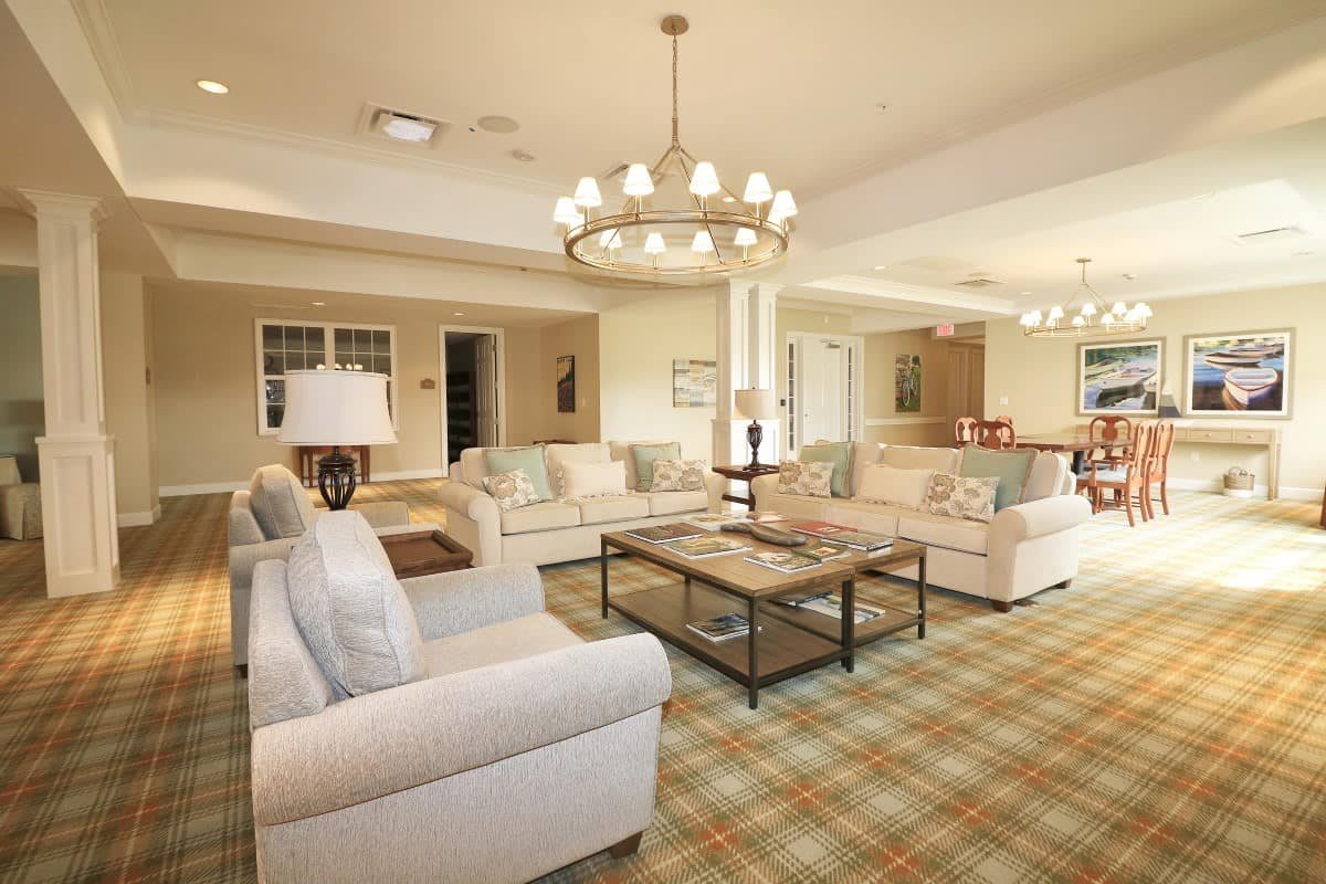 A spacious and elegantly designed living room featuring comfortable sofas, a central coffee table, and a stylish chandelier, all set on a patterned carpet.
