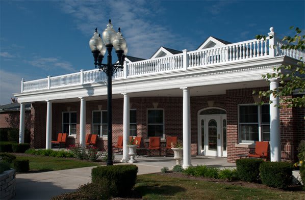 A brick building with white columns and a balcony, featuring outdoor seating and a lamppost.