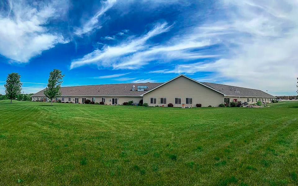A wide, single-story building surrounded by a grassy lawn under a blue sky with wispy clouds.