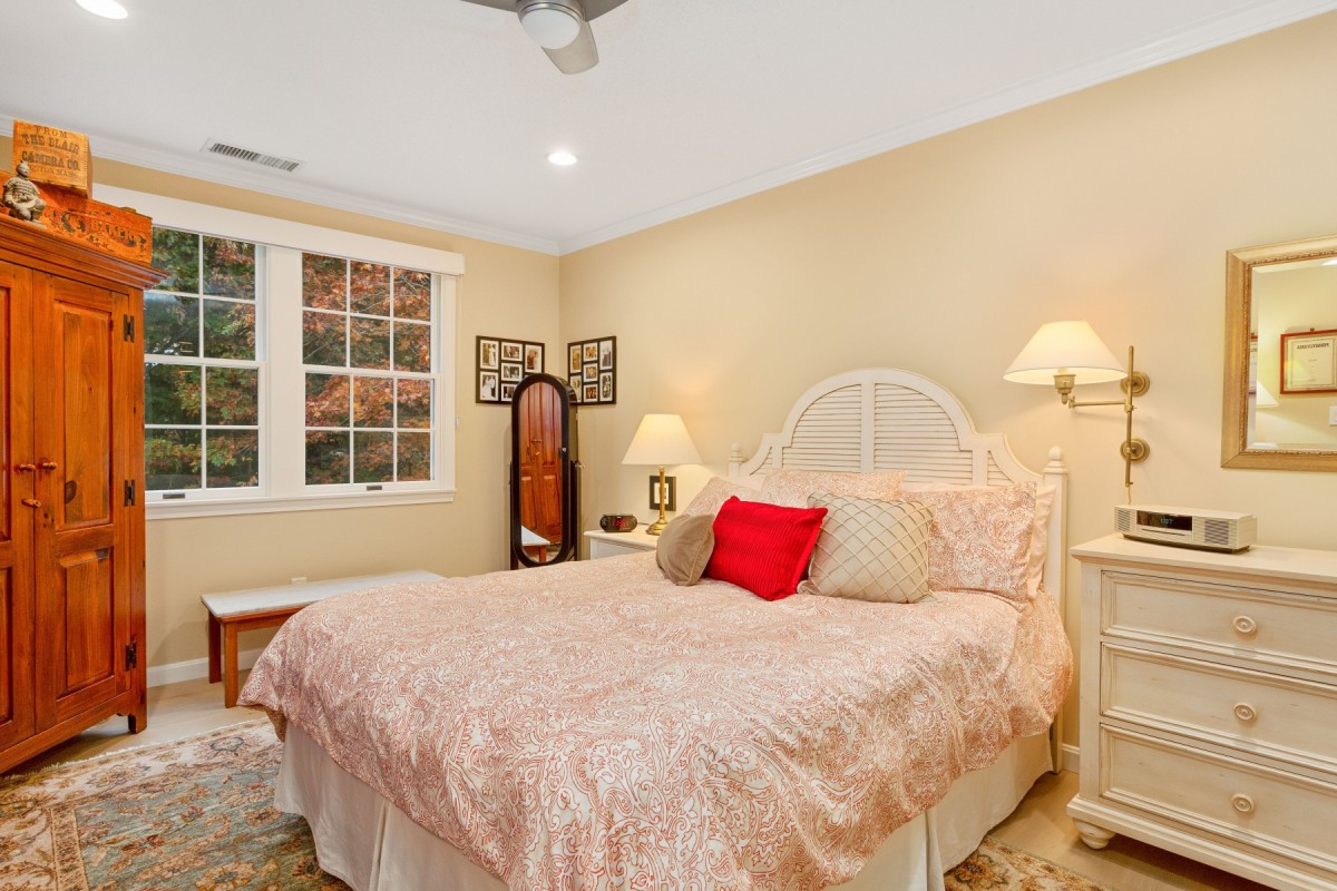 A cozy bedroom with a bed adorned with pink bedding, nightstands with lamps, and a mirror next to a window.