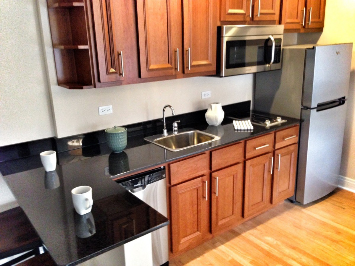 A modern kitchen with wooden cabinets, stainless steel appliances, and a black countertop.