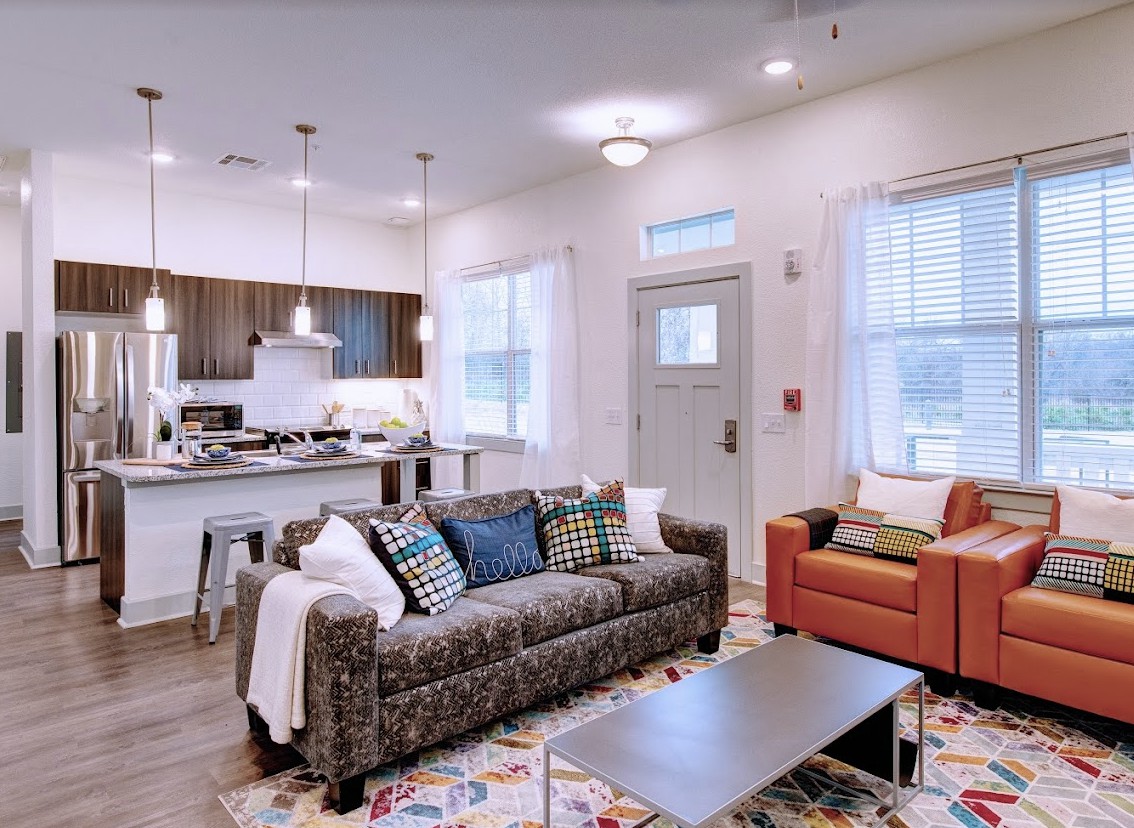 A modern living room with an open kitchen view, featuring a comfortable sofa, armchair, and stylish decor.