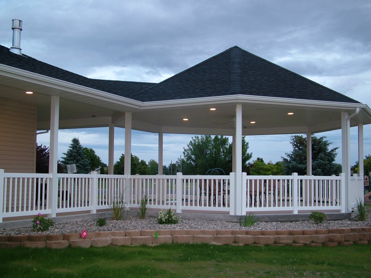 A large gazebo with a dark roof and white railings set in a garden area.