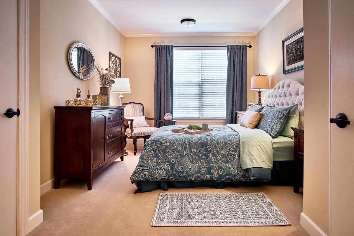 A cozy bedroom with elegant decor, featuring a bed, dresser, mirror, and lamps.
