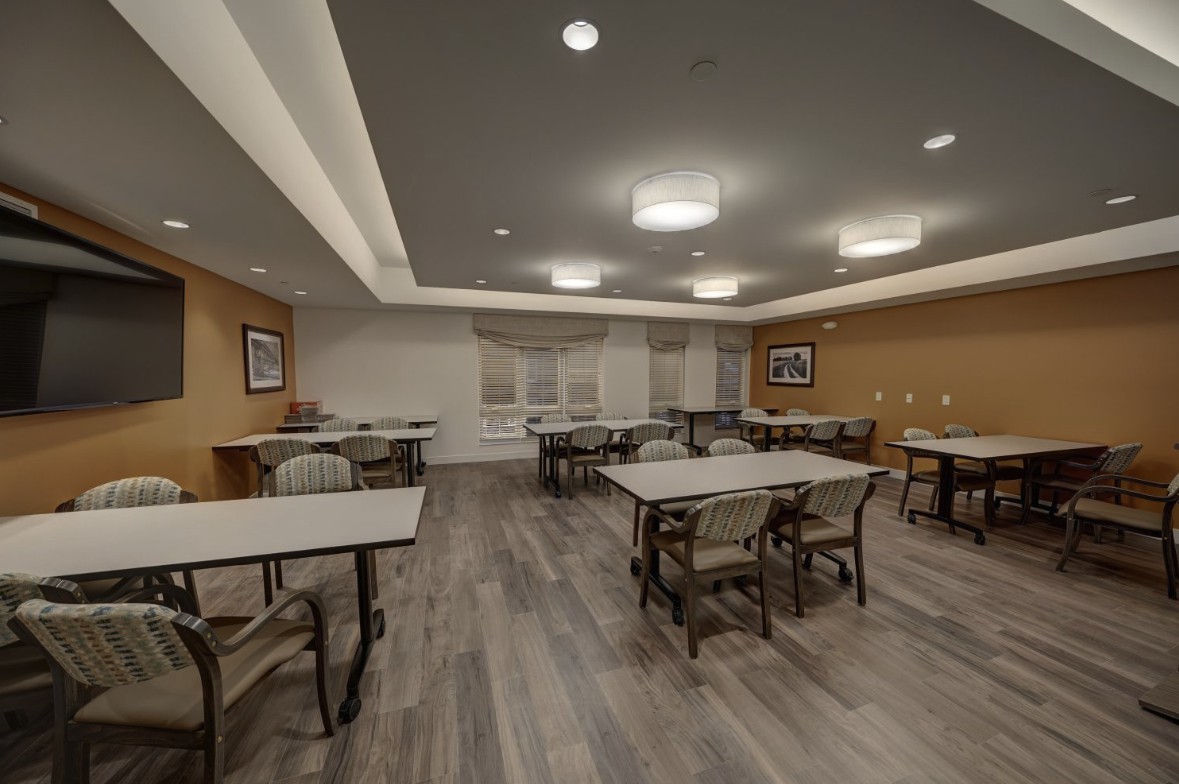 A spacious meeting room with multiple tables and chairs arranged under bright lighting.