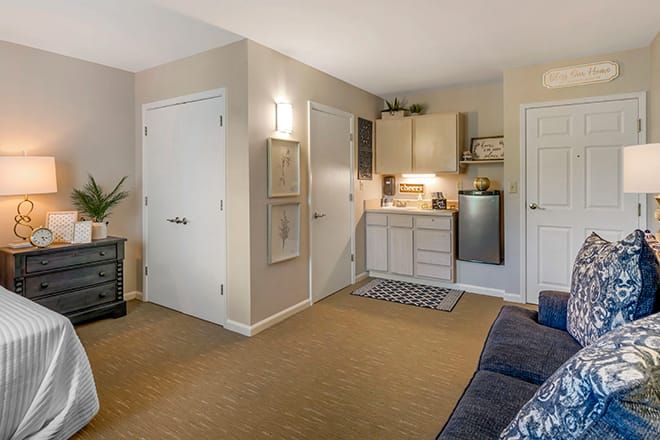 A modern apartment interior featuring a living area with a kitchenette and carpeted flooring.