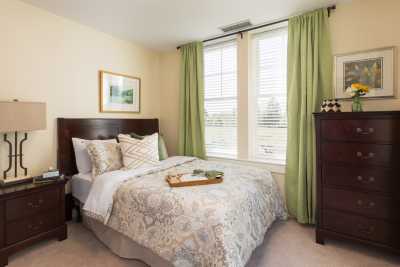 A cozy bedroom with a neatly made bed, green curtains, and a framed picture on the wall.