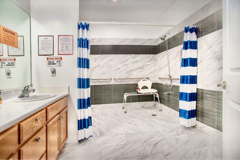 A spacious, accessible bathroom with a shower chair, blue and white striped curtains, marble tiles, and safety grab bars.