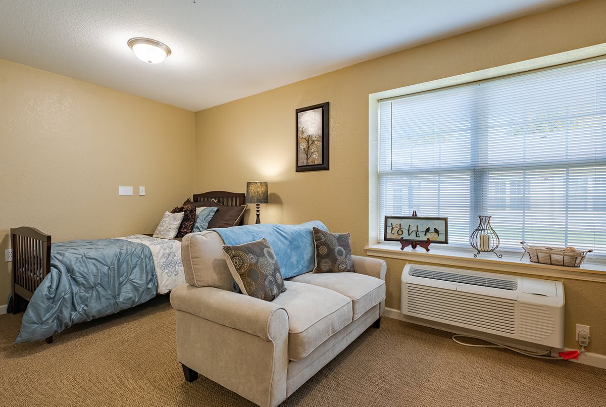 A cozy bedroom with a sofa, bed, and window providing natural light.