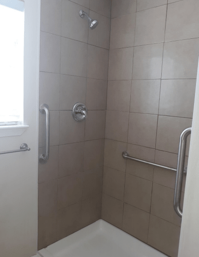 A tiled bathroom shower with grab bars installed.