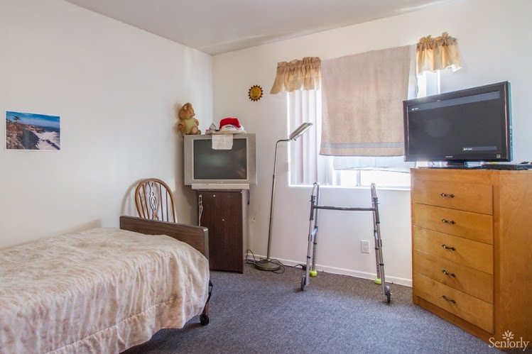 A small bedroom with a bed, TV, chair, and a ladder near the window.