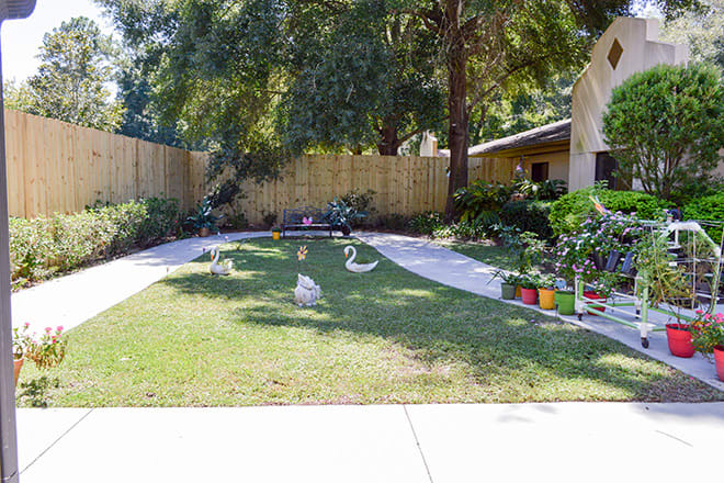 A well-maintained garden with grass, plants, and decorative sculptures bordered by a wooden fence.