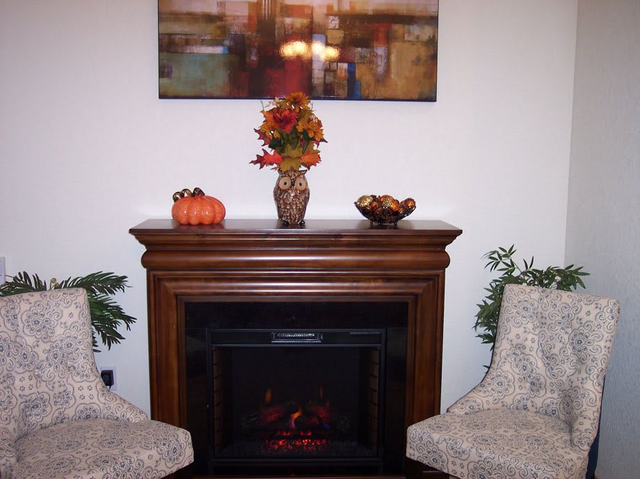 A cozy indoor setting featuring a decorative fireplace adorned with autumn-themed decorations, including a vase of flowers and a small pumpkin.