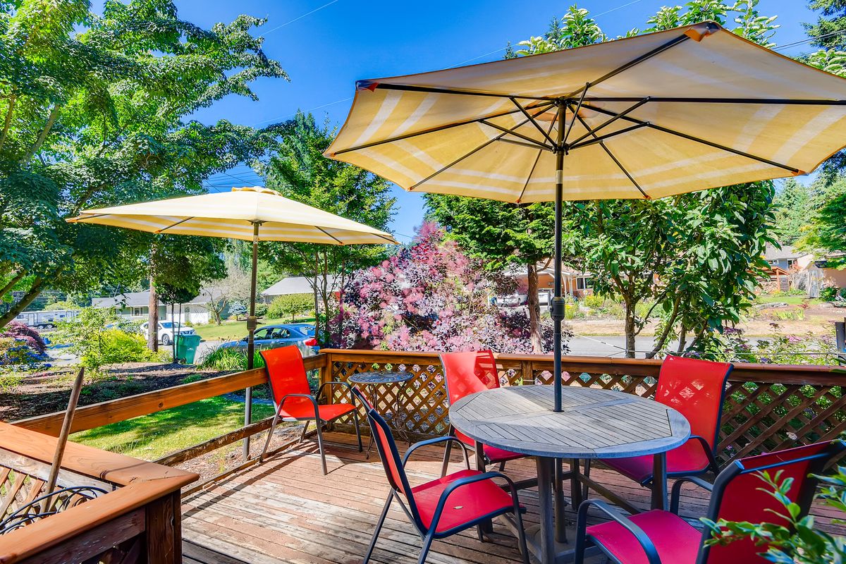 A sunny outdoor patio with tables and umbrellas surrounded by greenery.
