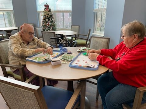 Two elderly individuals engaged in a crafting activity at a table indoors.