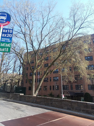 A bus stop with route information in an urban setting, featuring a tree and a nearby building.