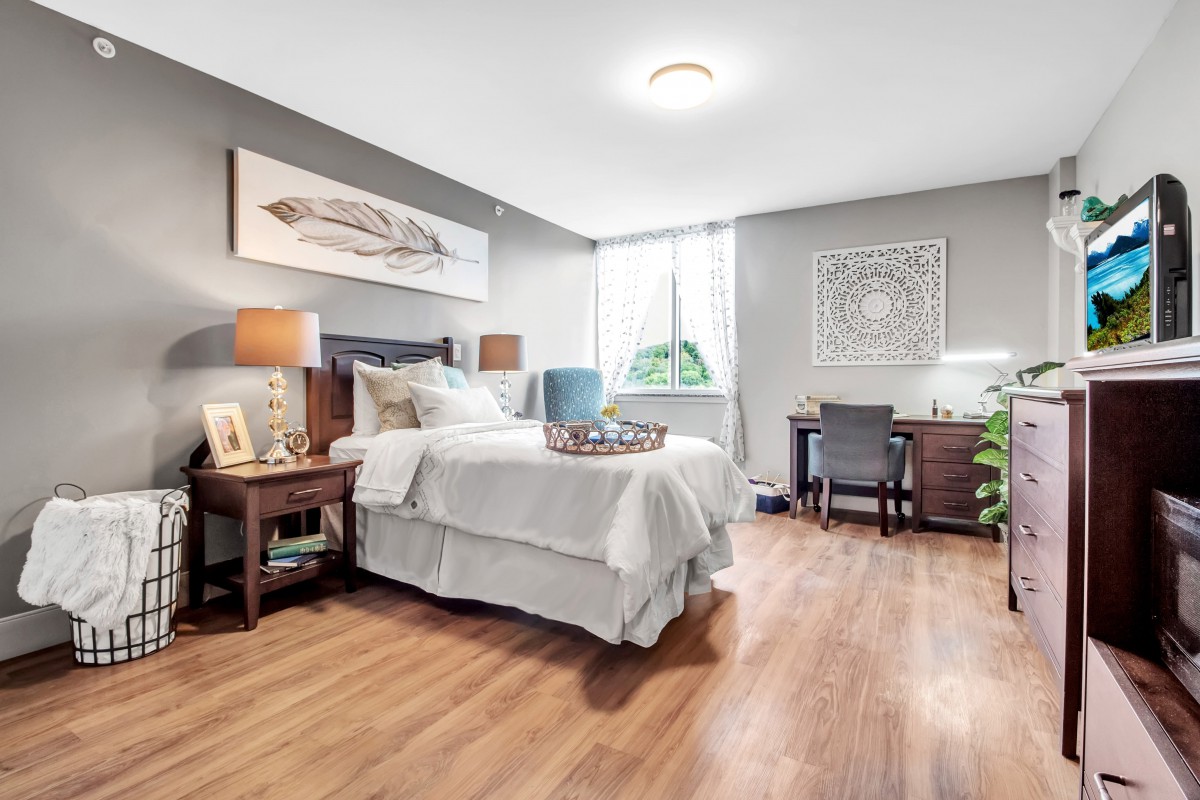 A cozy and well-decorated bedroom with a bed, desk, and wooden flooring.