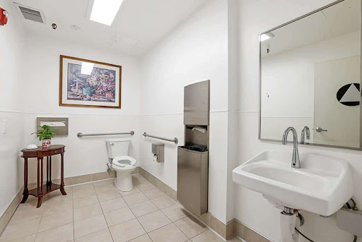 A clean and modern accessible bathroom featuring a toilet, sink, and artwork on the wall.