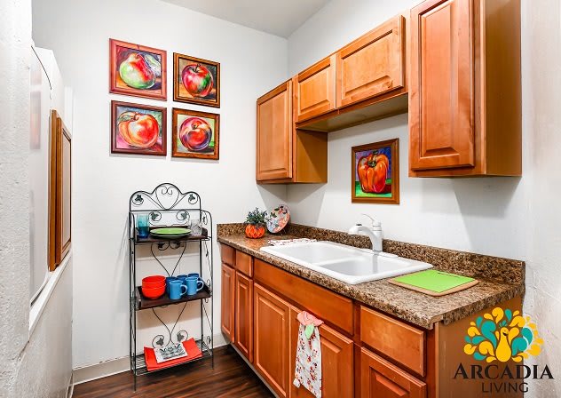 A cozy kitchen with wooden cabinets, colorful artwork, and neatly arranged shelves.