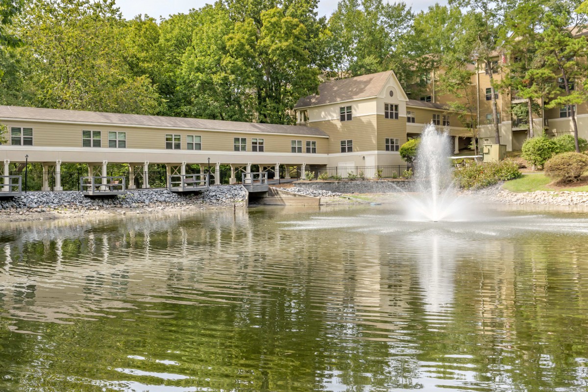 A serene lakeside view featuring a building with a fountain in the foreground and trees in the background.