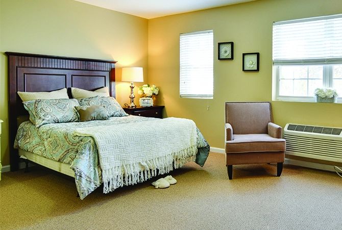 A cozy bedroom with a bed, armchair, and warm lighting.