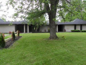 A single-story house with a large front lawn and a prominent tree.
