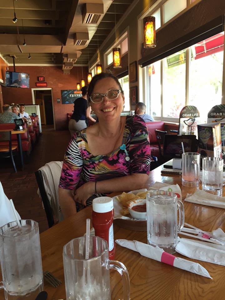 A person sitting at a table in a restaurant with drinks and condiments.